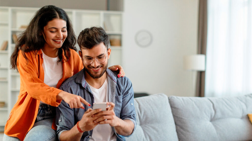 Casal lado a lado em um sofá interagem em um celular